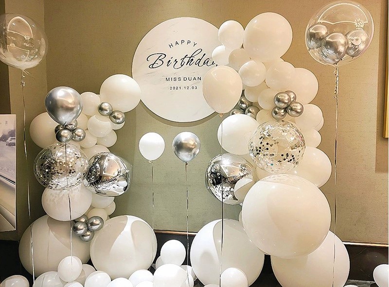 The Elegant Silver and White Birthday Balloon Decoration Setup from Valentine-day.shop includes white, silver, and confetti-filled clear balloons in various sizes around a circular Happy Birthday wall sign with a date.