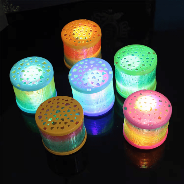 A group of six colorful Bluetooth speakers with vibrant blue, green, yellow, and pink lights sits on a dark surface, resembling Mini Rainbow LED Bounce Spring Toys. Decorative cut-out designs enhance their tops.