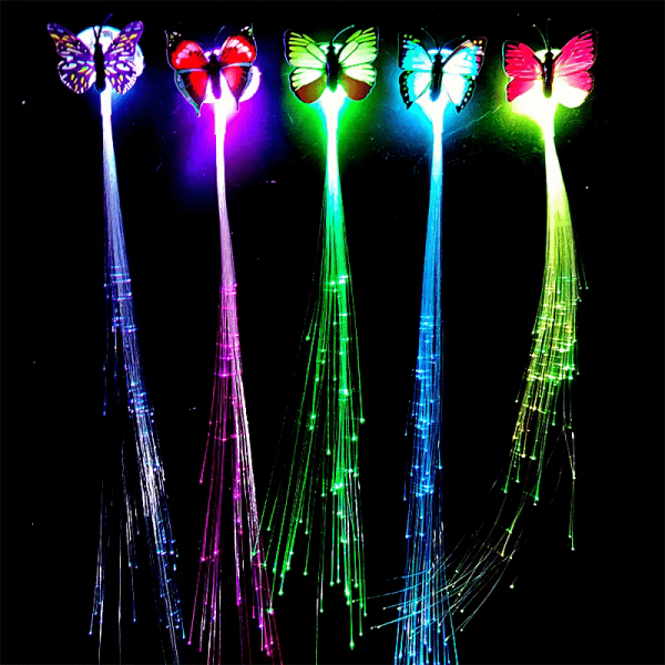 Five vibrant fiber optic wands, similar to LED Hair Extensions, lie on a black backdrop with glowing butterflies in purple, red, green, blue, and pink hues atop them. Matching fiber optic strands flow elegantly beneath each butterfly.