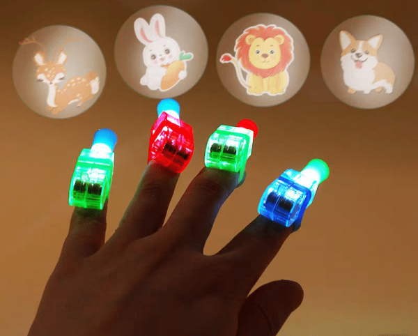 A hand with LED Cartoon Character Finger Rings projects vivid animal images like a deer, rabbit with a carrot, lion, and corgi against a dark background, enhancing the colorful projections and glow of the rings.
