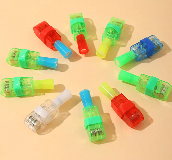 A playful pattern emerges as colorful plastic whistle toys with transparent tops and solid cylindrical mouthpieces are arranged in a circle on a light orange background. Interspersed among them, LED Cartoon Character Finger Rings add whimsy to the red, green, blue, and yellow palette.