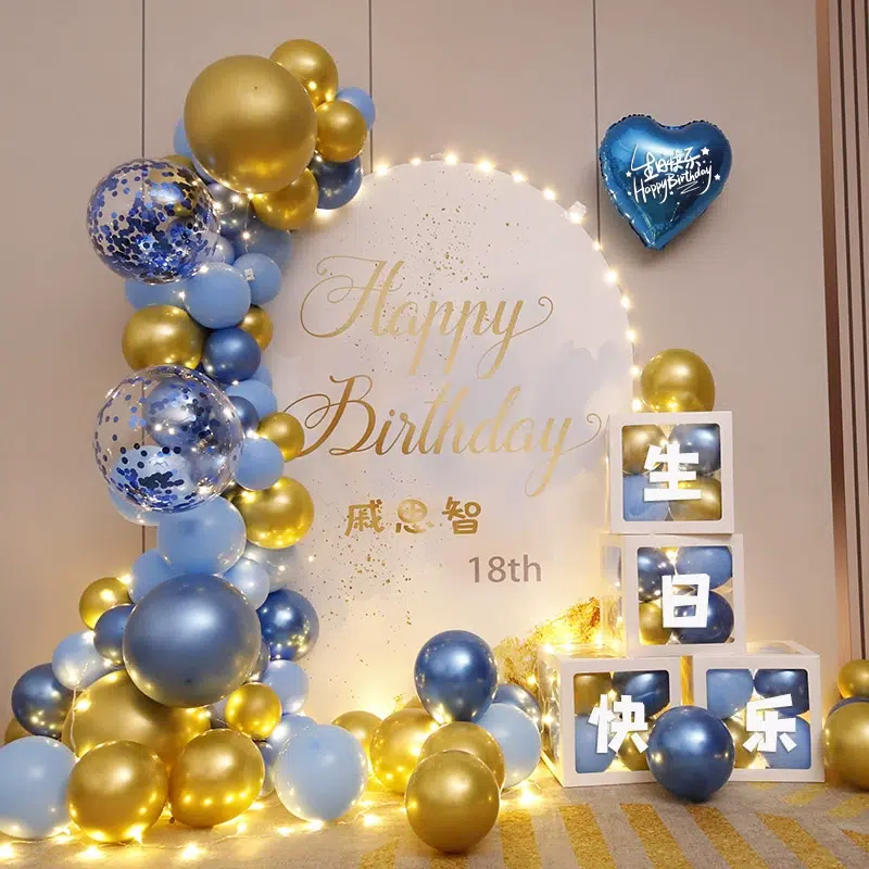 A Happy Birthday display with a circular backdrop, surrounded by blue and gold balloons. Illuminated blocks spell out 生日快乐 in Chinese, meaning Happy Birthday. Theres a blue heart-shaped balloon with Happy Birthday written on it.